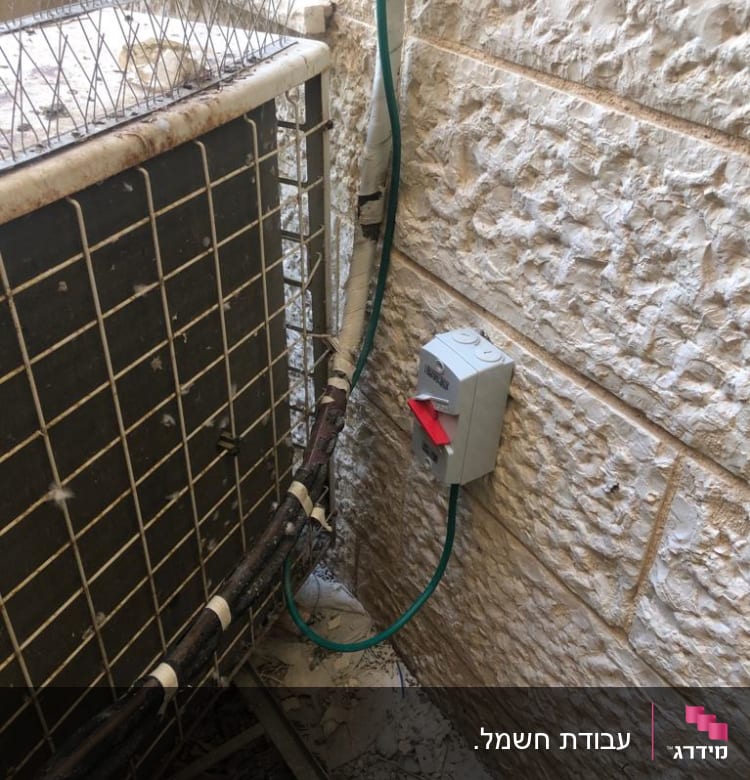 מתג חשמלי על קיר אבן עם חוטים ירוקים